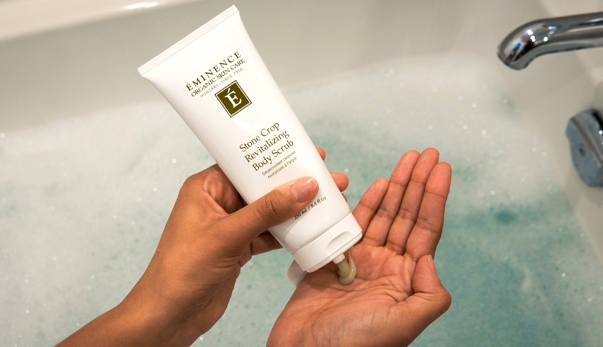 a woman squeezing Stone Crop Revitalizing Body Scrub from a lotion bottle into her hand